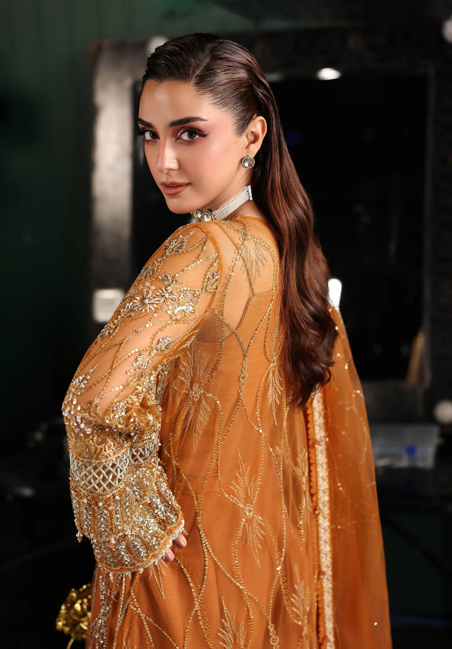 Woman in an orange embroidered outfit with Elaf Stardom Handwork.