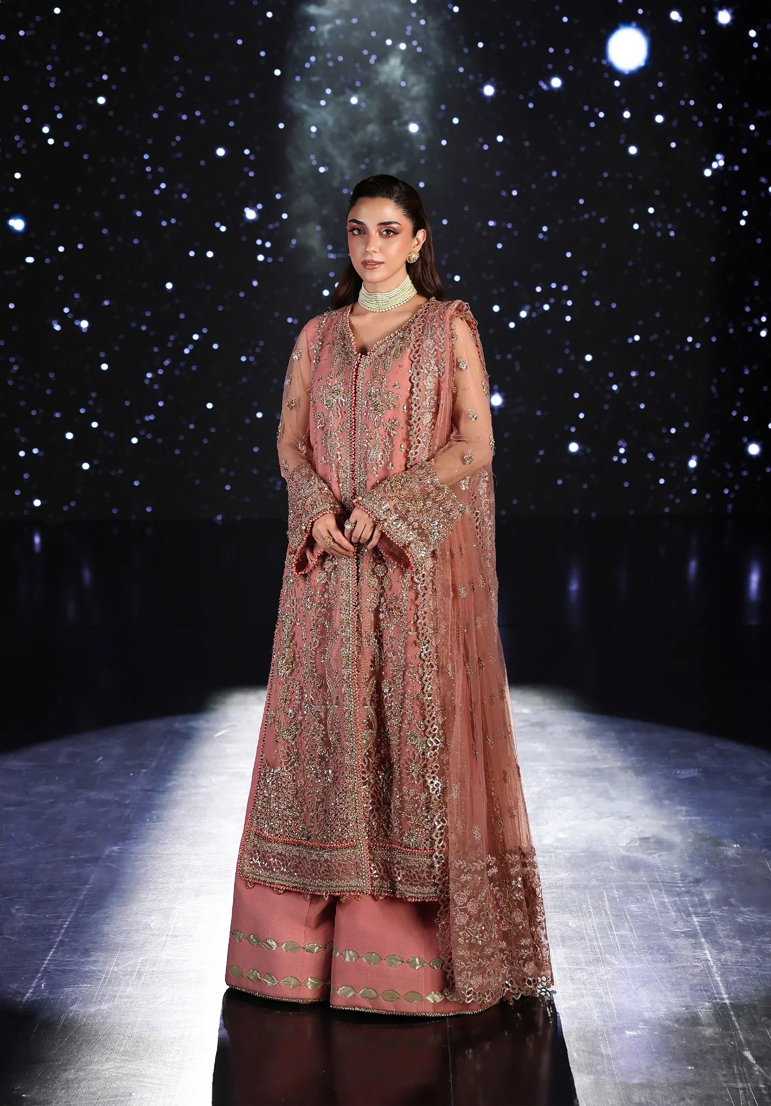 Woman in a traditional pink embroidered outfit on a dark background with star-like lights