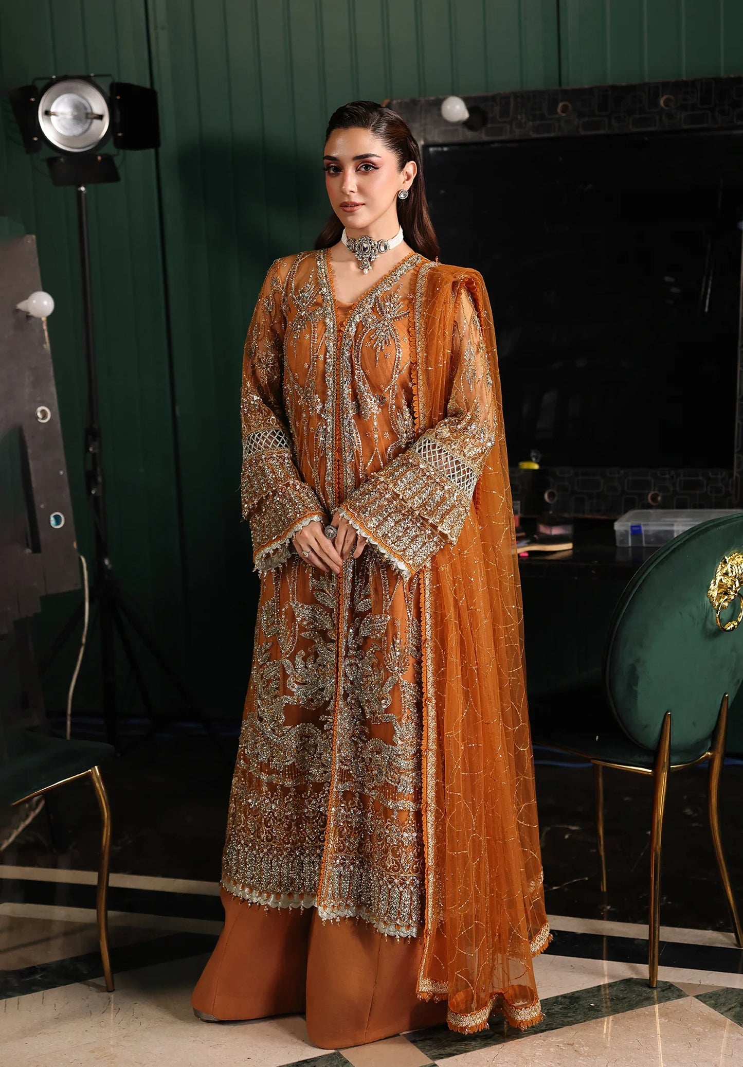 Woman in a traditional outfit standing in a room with green walls and a fireplace with Elaf Stardom Handwork.