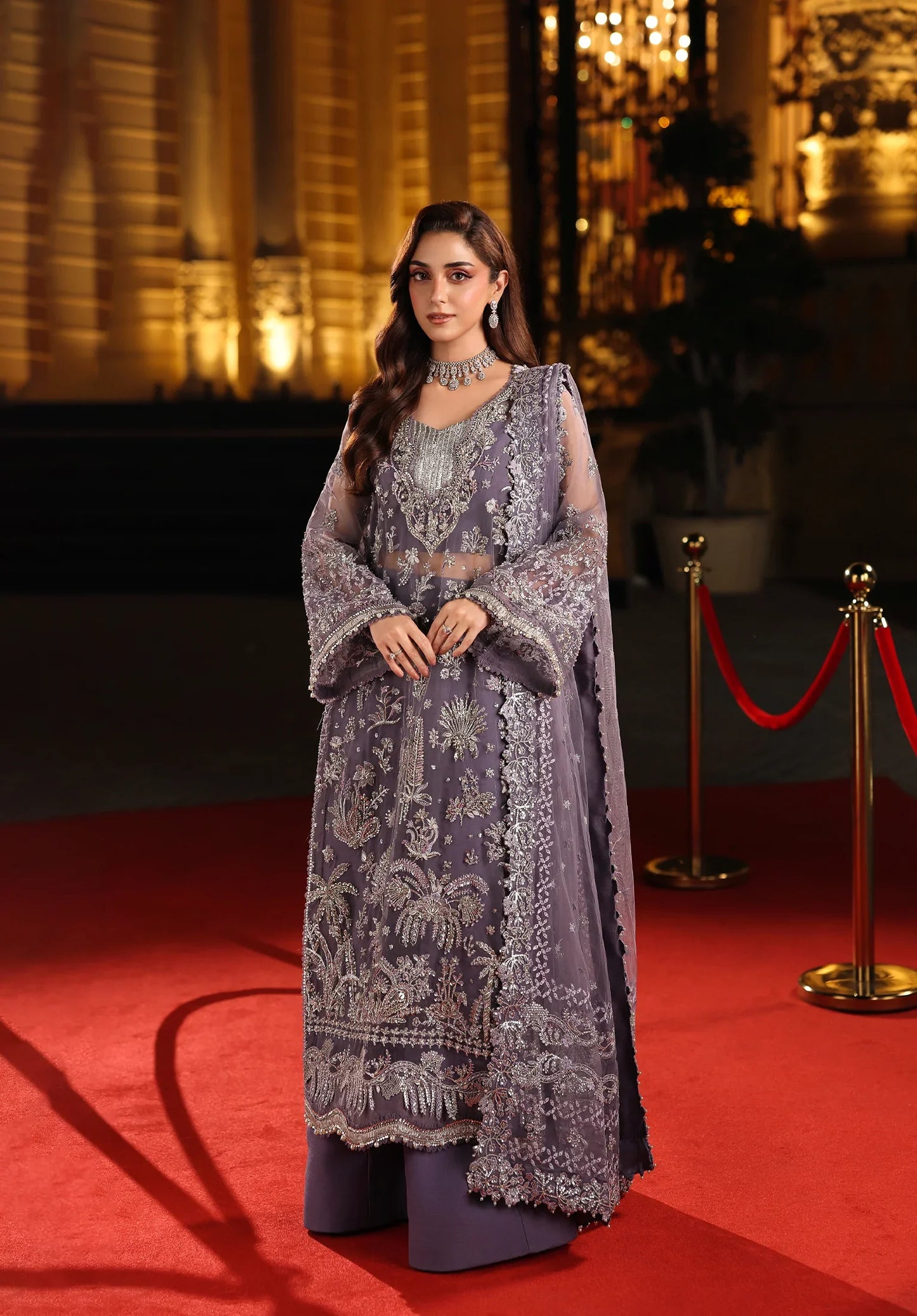 Woman in a traditional outfit on a red carpet with a blurred background