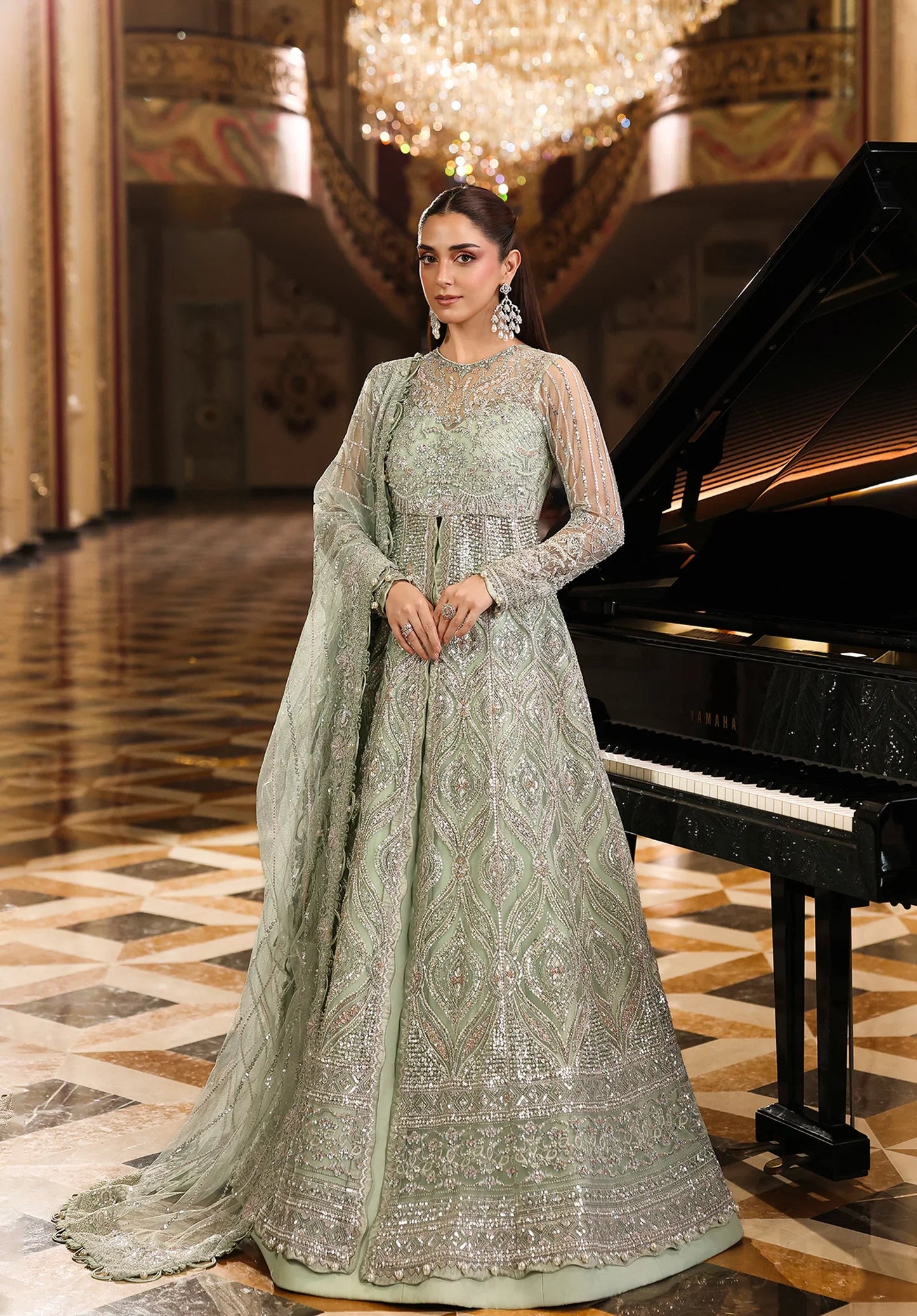 Woman in a light green embroidered traditional outfit standing next to a grand piano in an elegant room.