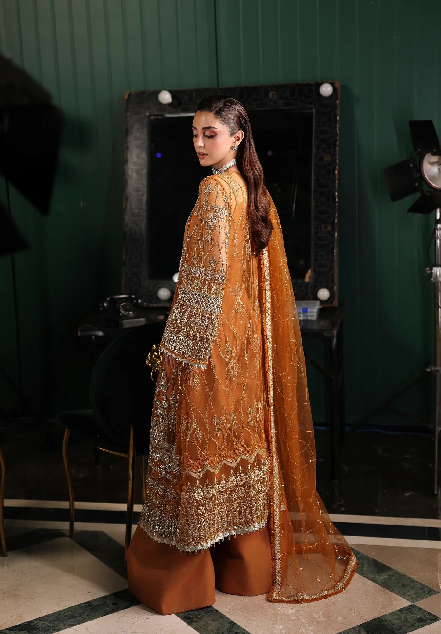 Woman in a traditional mustard yellow and white embroidered outfit standing in a room with green walls and a mirror.